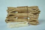 Three coiled bundles of natural jute shibari rope stacked together with the kit's cream drawstring storage pouch